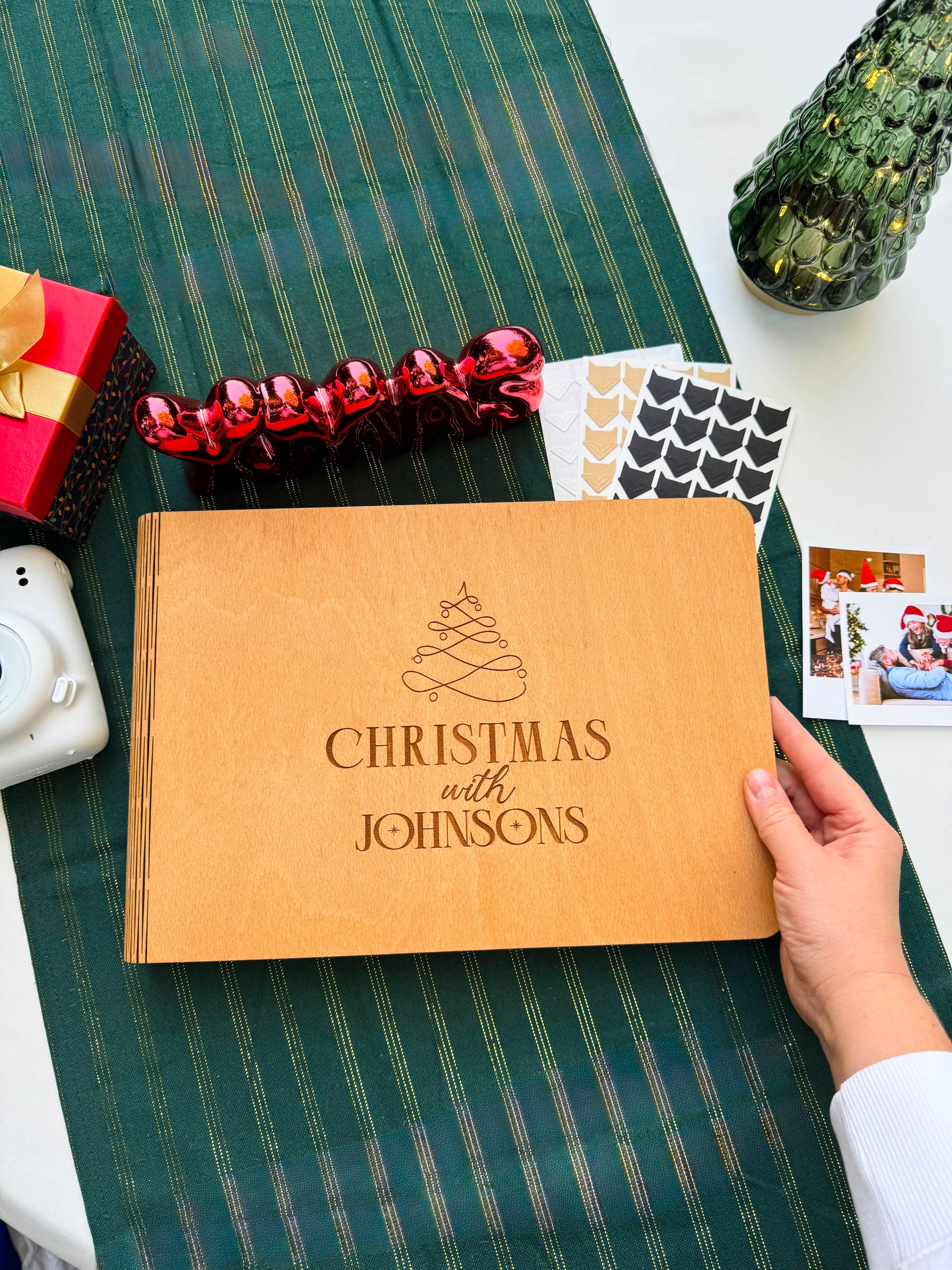Personalized wooden Christmas photo album engraved with family name on a green tablecloth with festive decorations.
