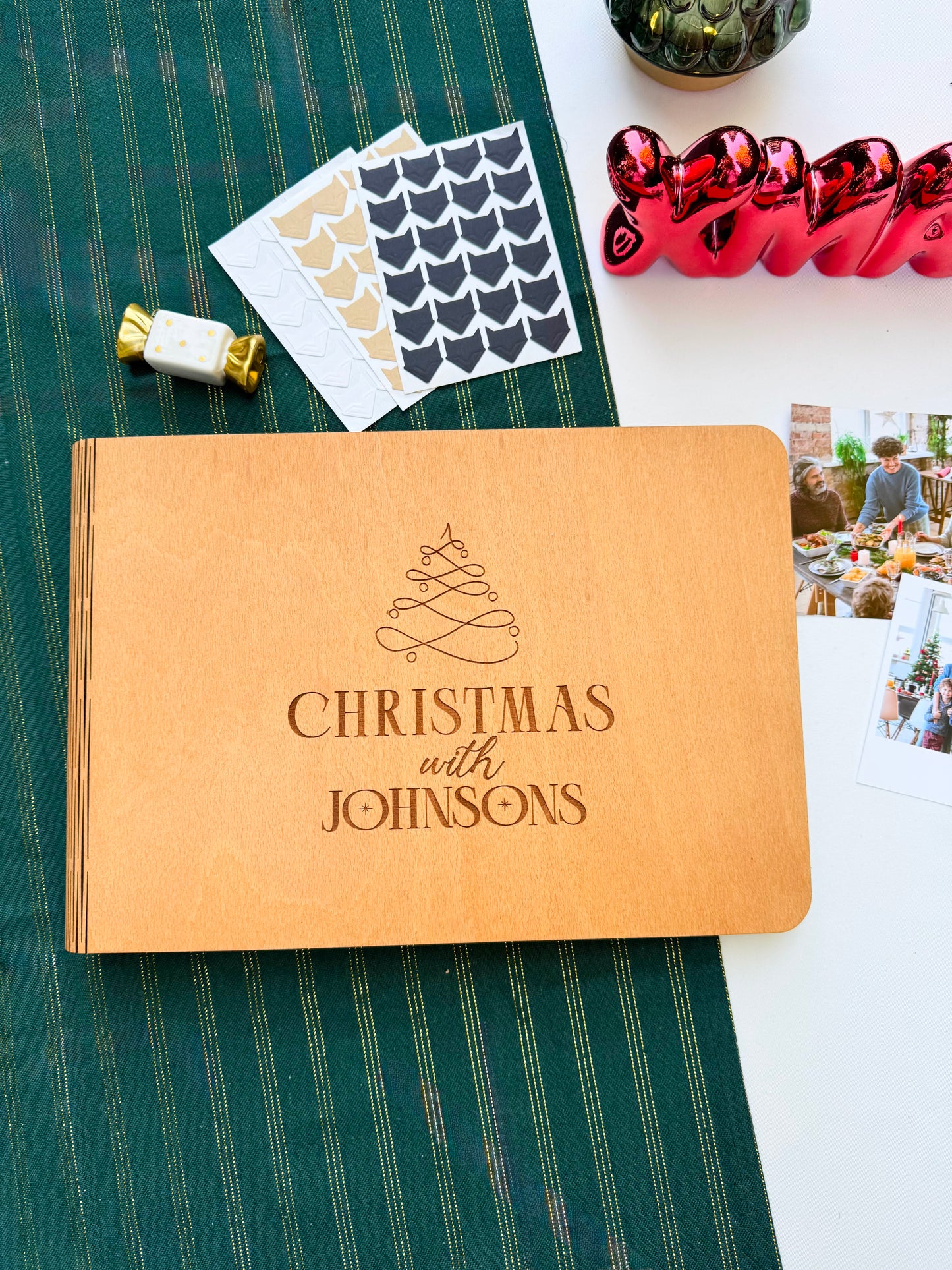 Personalized wooden Christmas photo album engraved with family name on a green tablecloth with festive decorations.
