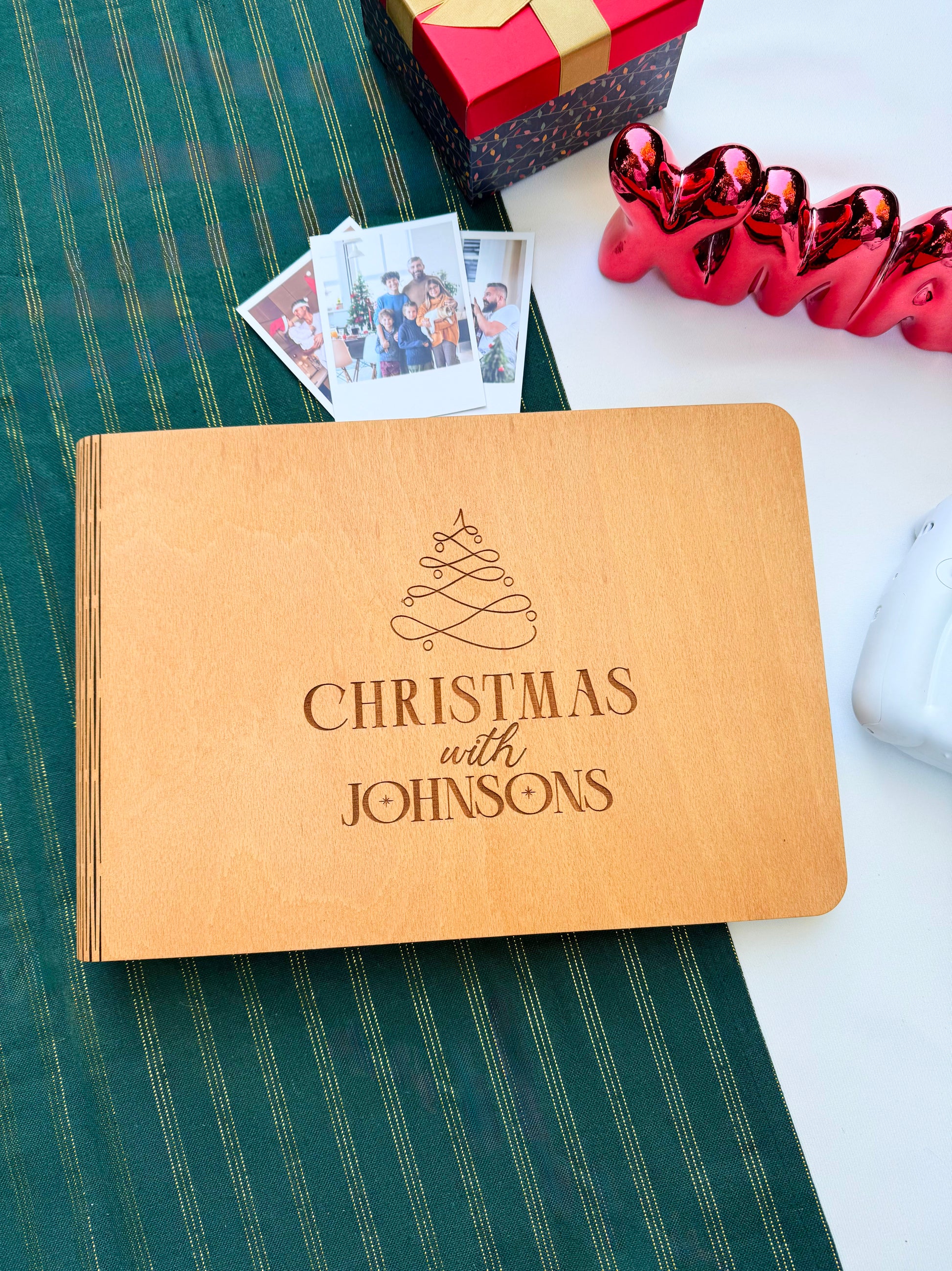 Personalized wooden Christmas photo album engraved with family name on a green tablecloth with festive decorations.
