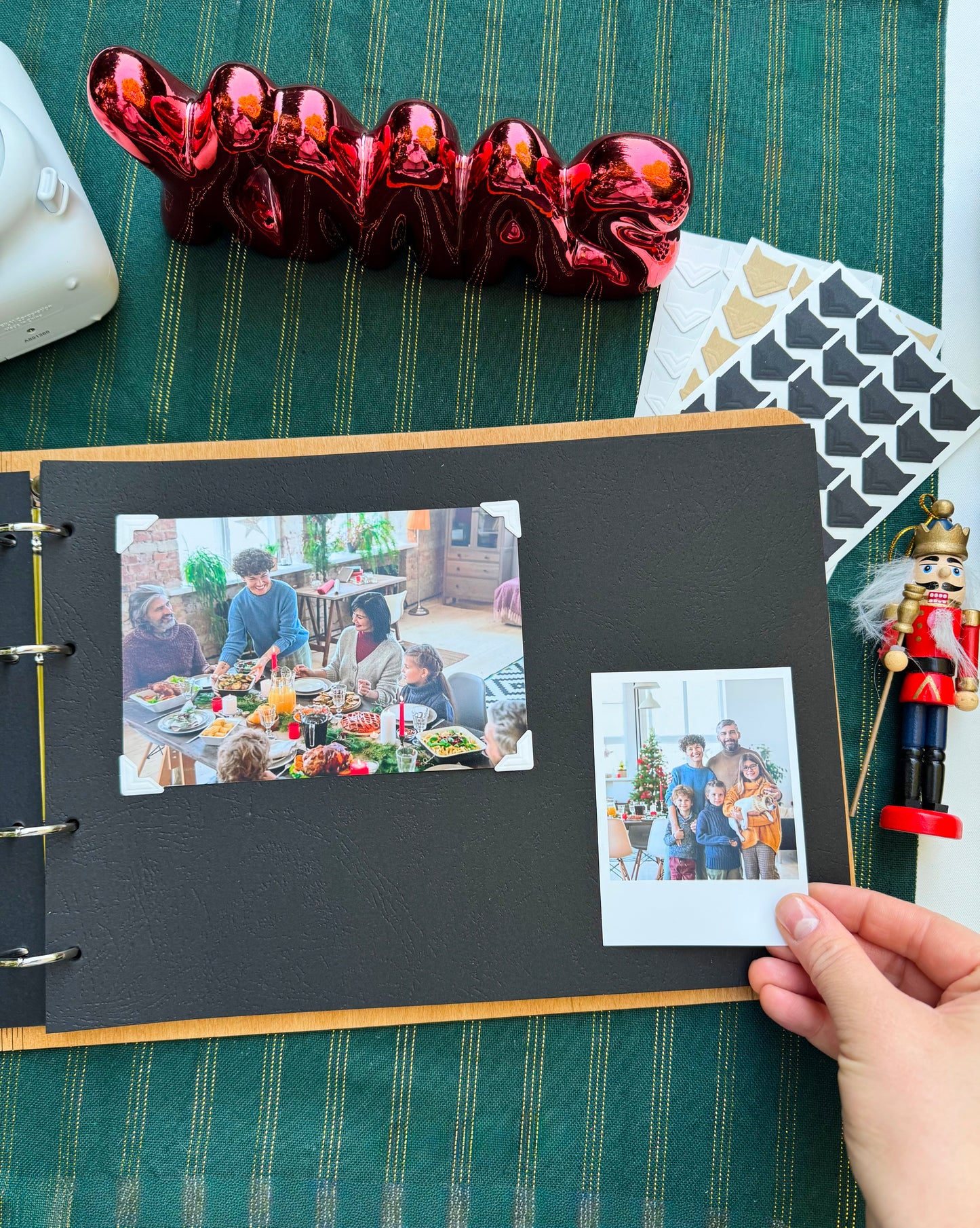 Open personalized wooden Christmas photo album with family Polaroid photos on a green tablecloth and festive decor.
