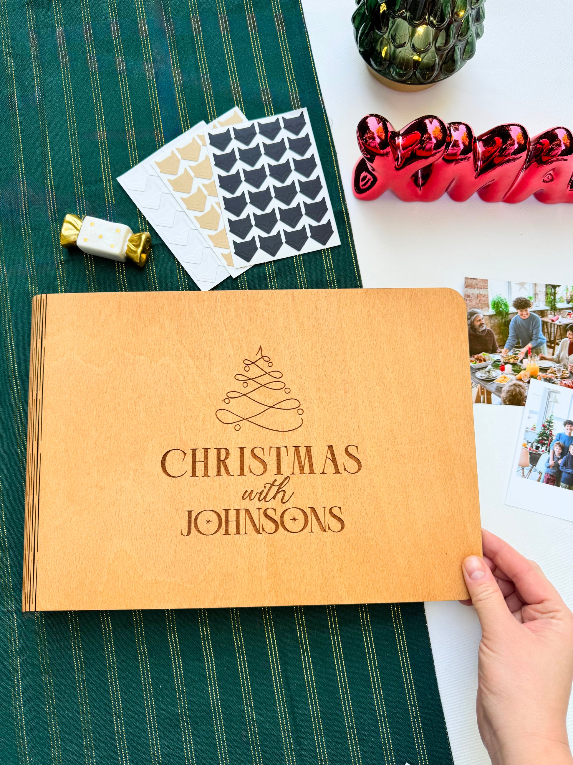 Personalized wooden Christmas photo album engraved with family name on a green tablecloth with festive decorations.
