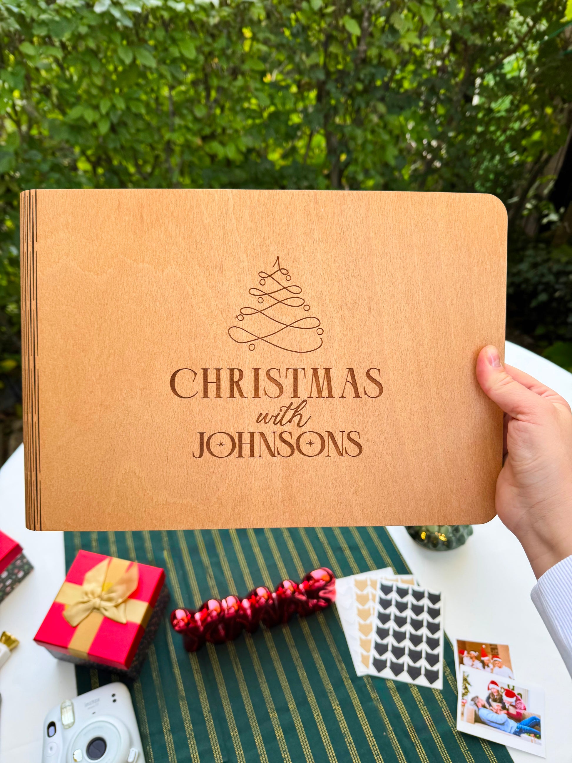 Personalized wooden Christmas photo album engraved with family name on a green tablecloth with festive decorations.


