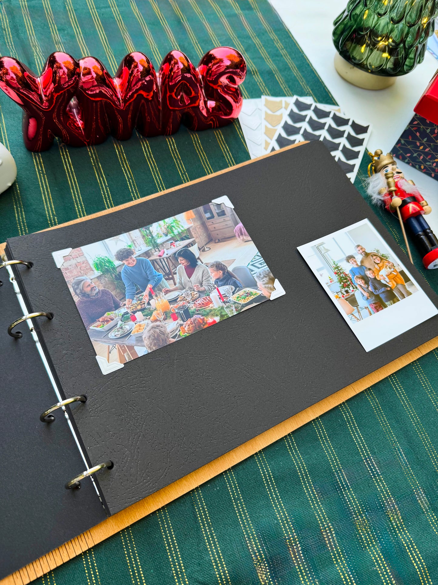 Black photo album with open pages showing family photos on a green tablecloth.